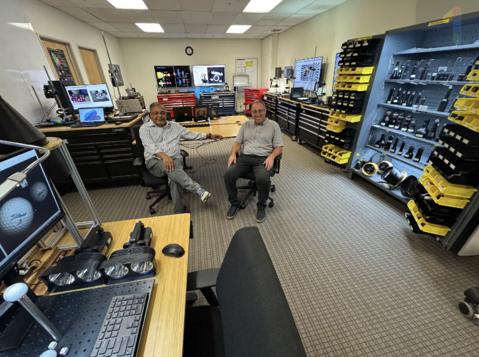 Two men sitting in chairs in a room with computers and electronics

Description automatically generated